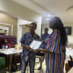 At a doctor's office in Abuja, a woman proudly holds a certificate in front of a group of people.